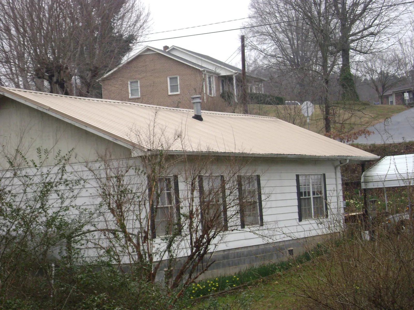 Tan metal roof on a white sided house set into a hillside — Commercial Roofing by Roofing Brothers in Lawndale